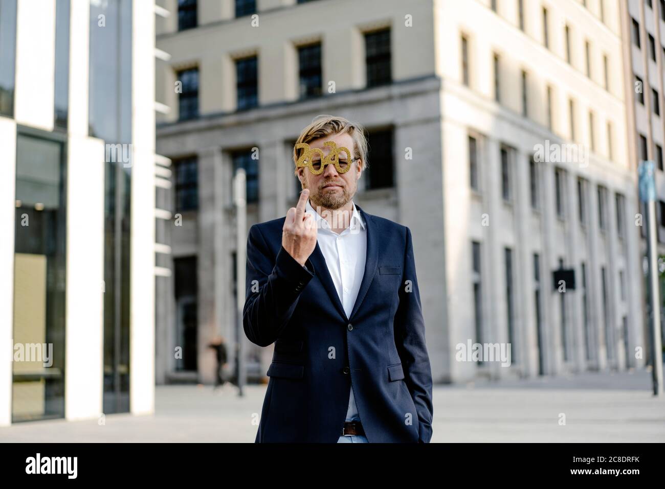 Uomo d'affari che indossa 2020 occhiali da commedia in città dando il dito Foto Stock