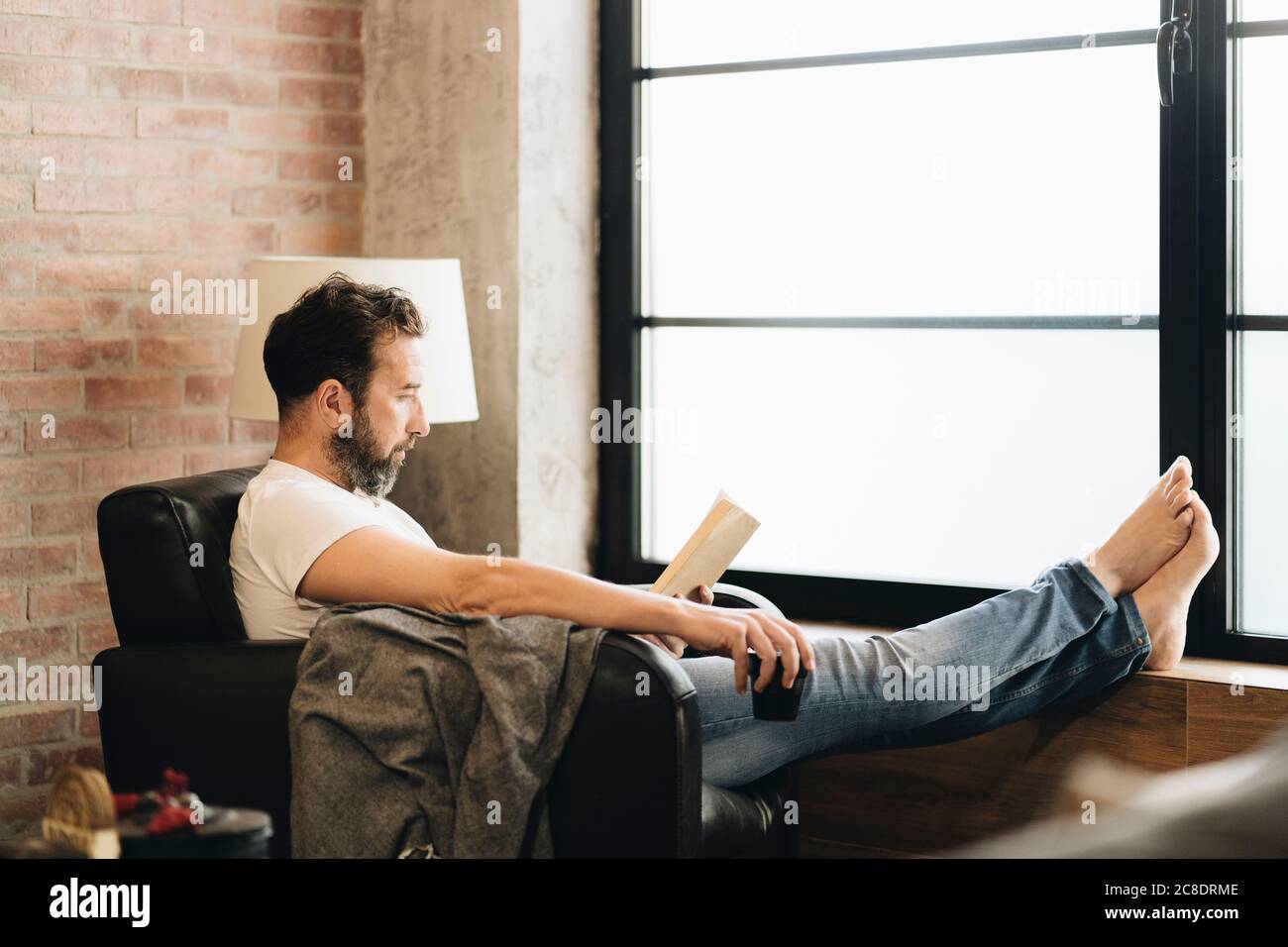 Uomo maturo seduto a piedi nudi in poltrona, lettura bok Foto stock - Alamy