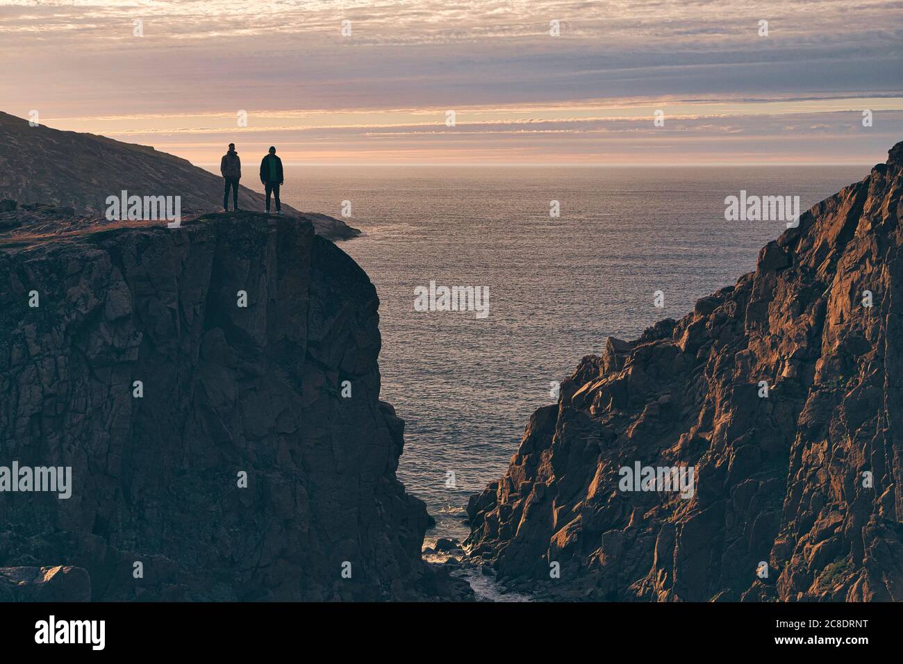 Uomini silhouette in piedi sulla scogliera durante il tramonto a Teriberka, Murmansk Oblast, Russia Foto Stock