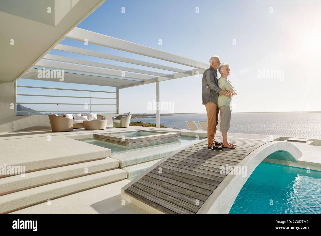 Affettuosa coppia anziana che si erge sul ponte sopra una piscina in una casa di lusso sulla spiaggia Foto Stock