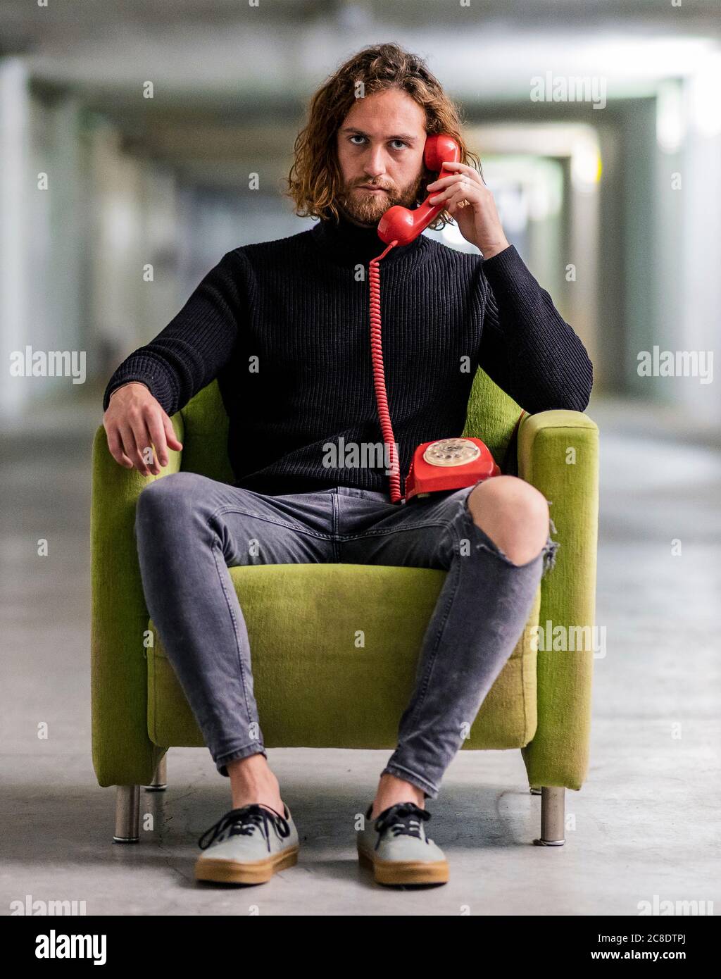 Un giovane serio che parla al telefono mentre si è seduti su una poltrona a casa Foto Stock