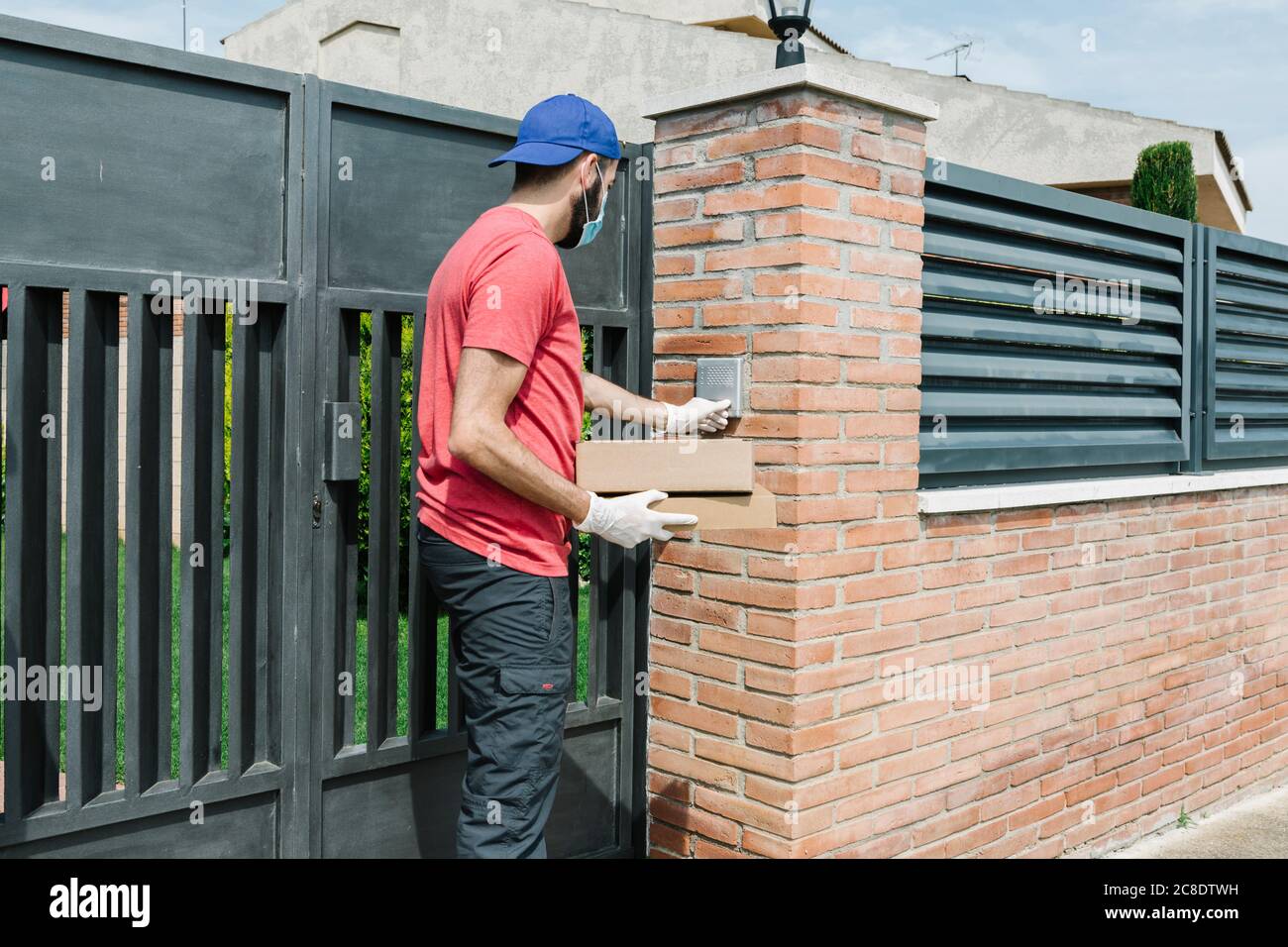 Persona di parto di sesso maschile di mezza età che usa l'interfono mentre si è in piedi con Pacchetto al gate durante COVID-19 Foto Stock