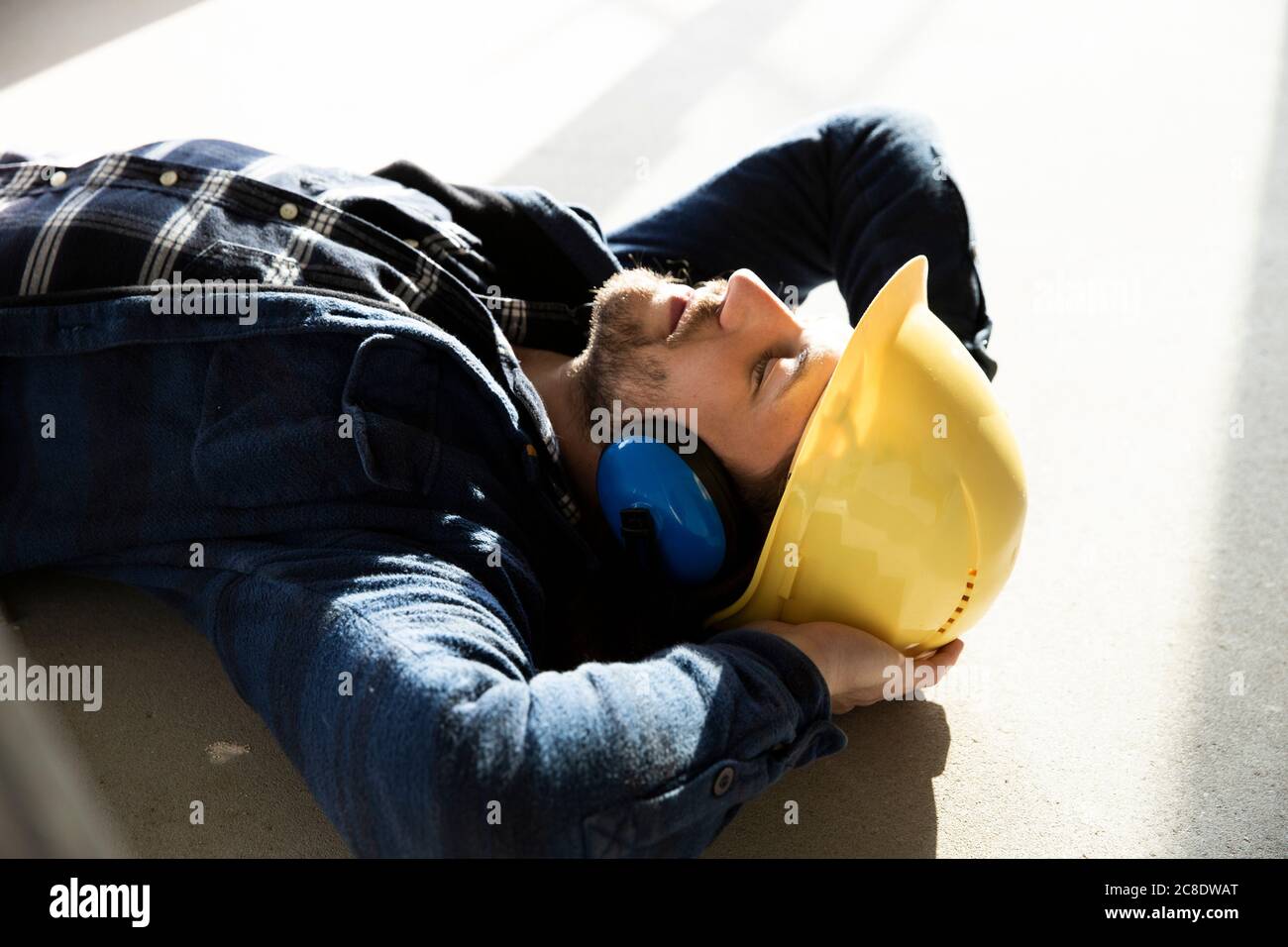 Primo piano del lavoratore di costruzione con le mani dietro la testa addormentate piano in casa di ristrutturazione Foto Stock