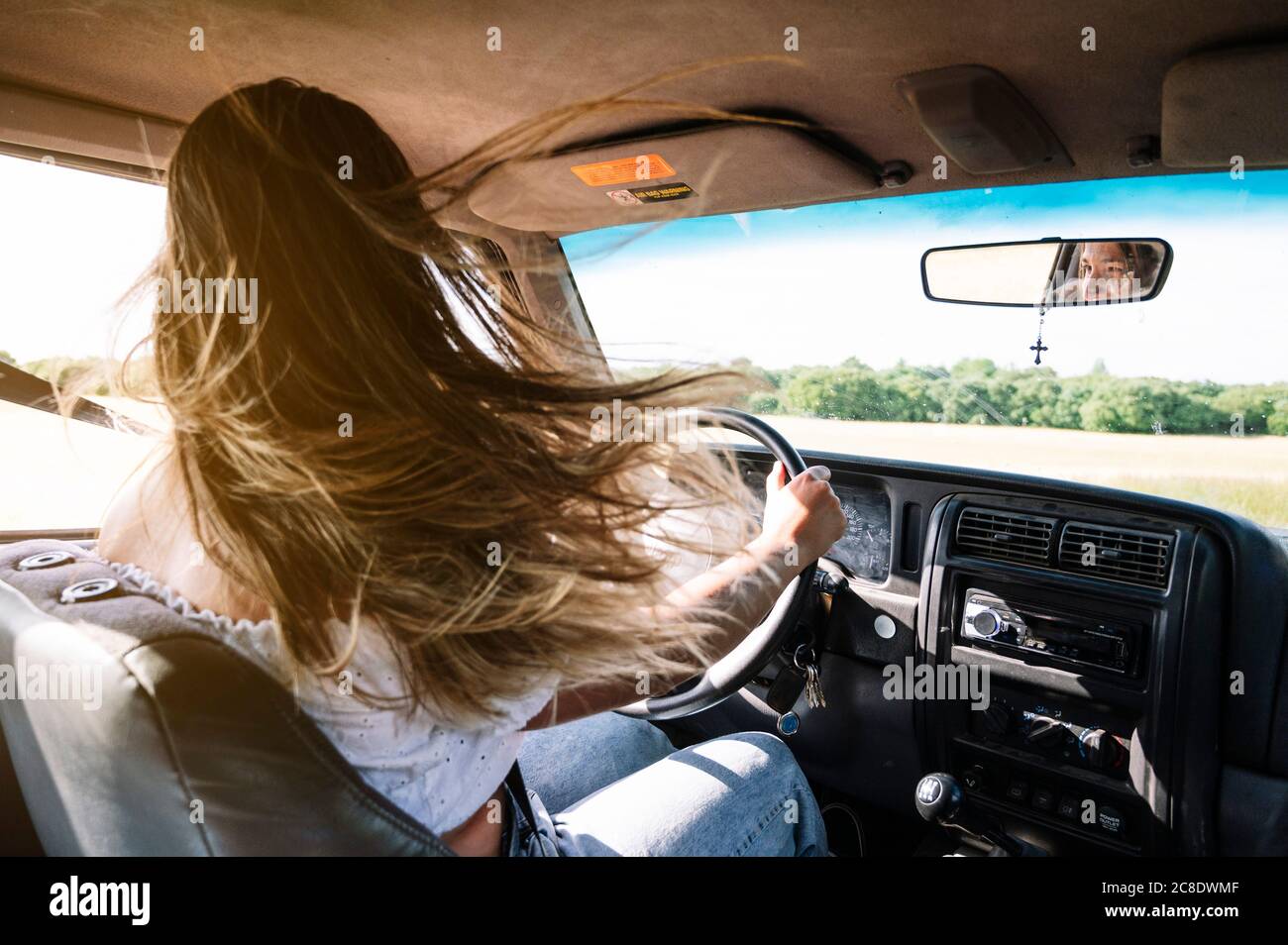 Donna con lunghi capelli biondi che guidano auto su strada viaggio Foto Stock
