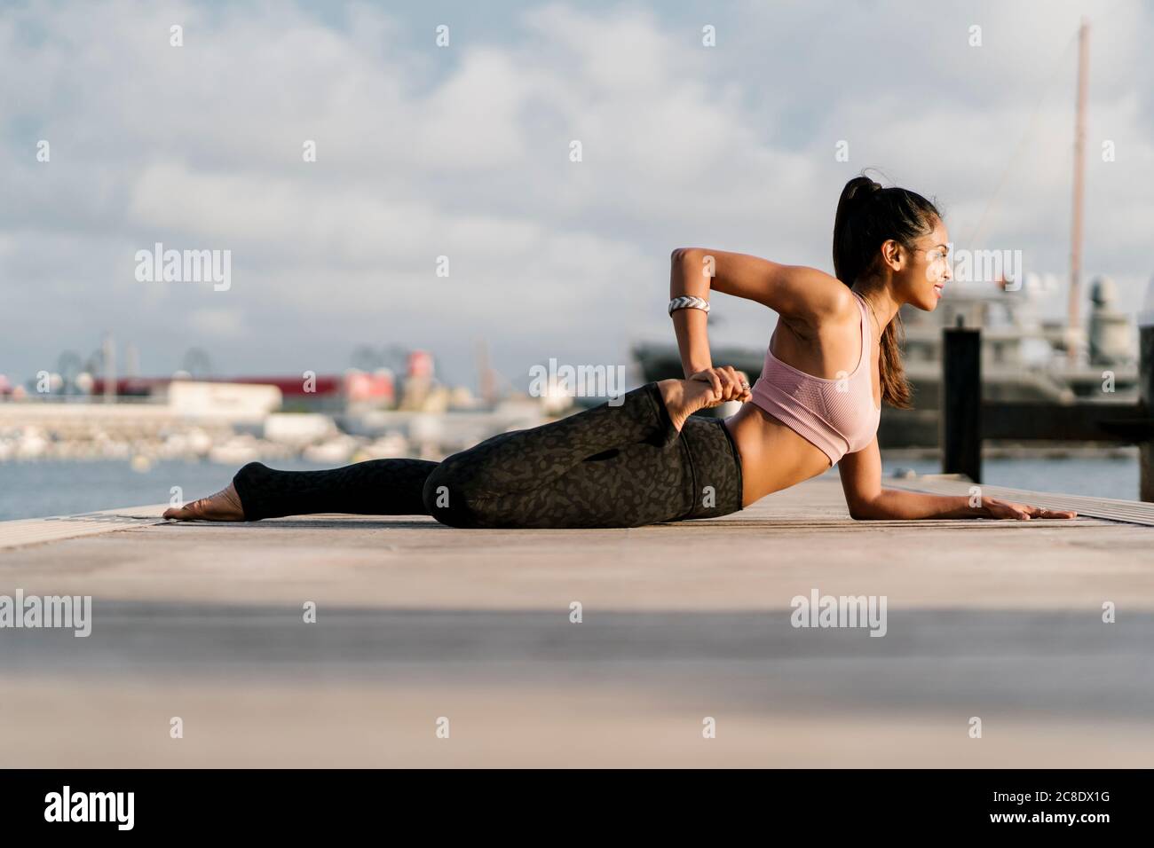 Atleta che pratica mezza rana posa sul molo al porto Foto Stock