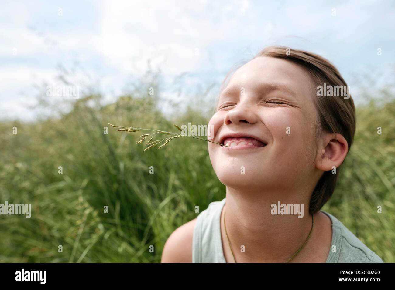 Ritratto di ragazzo con gli occhi chiusi tenendo lama d'erba con bocca Foto Stock