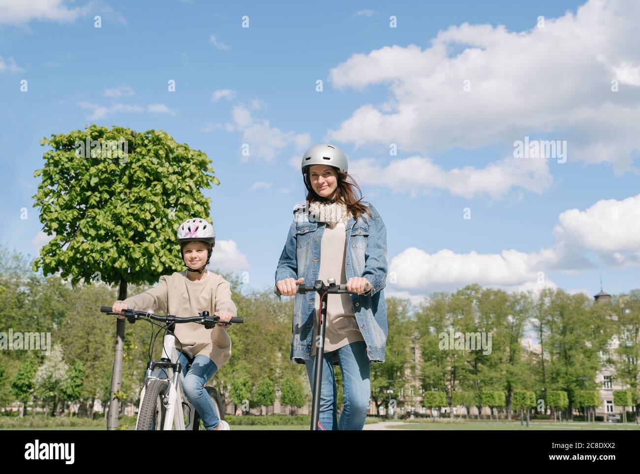 Ragazza in bicicletta mentre la madre cavalcava moto contro il cielo in città parcheggio Foto Stock