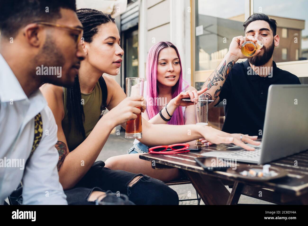 Gli amici bevono birra e usano il computer portatile all'aperto in un bar Foto Stock