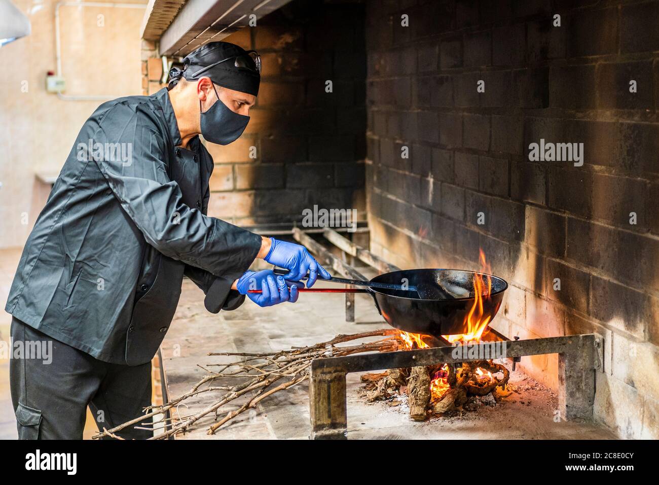 Cucina tradizionale di paella in cucina ristorante, chef con maschera protettiva Foto Stock