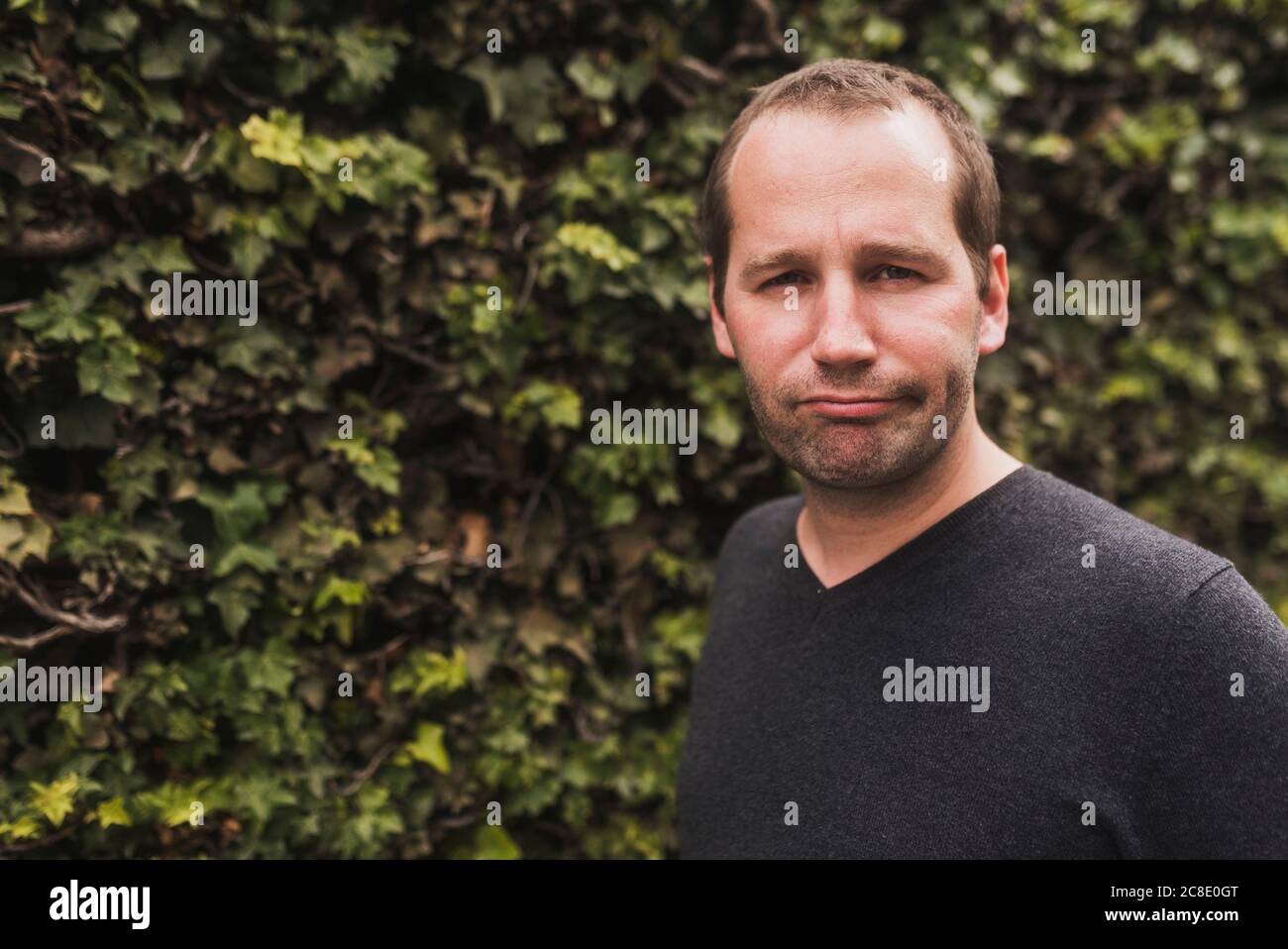 Primo piano di un uomo medio adulto che fa faccia contro le piante in parcheggio Foto Stock