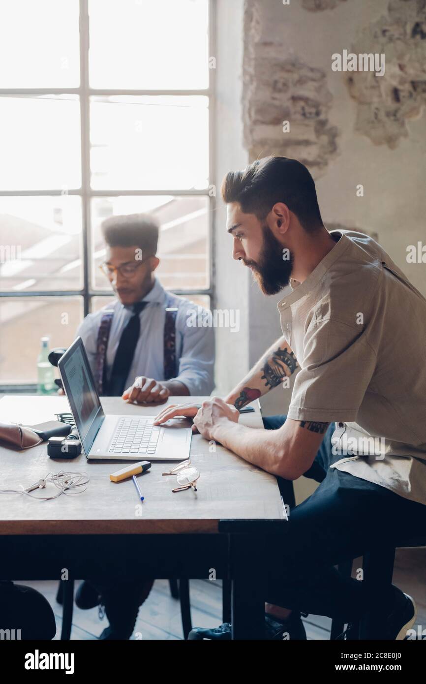 Uomini d'affari creativi che lavorano con il computer portatile al tavolo in loft ufficio Foto Stock