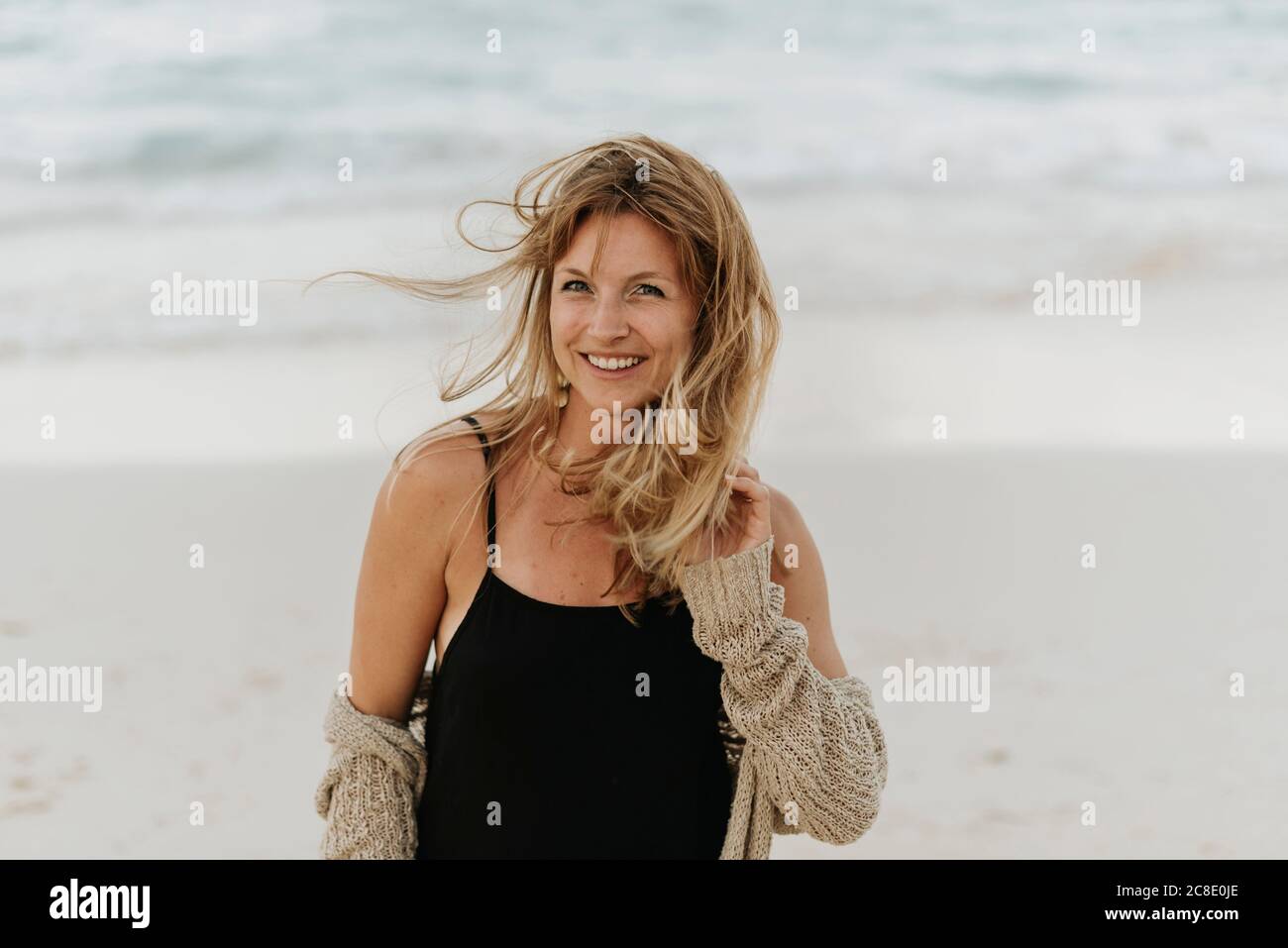 Ritratto di donna mid adulta sorridente con capelli biondi in piedi contro il mare Foto Stock