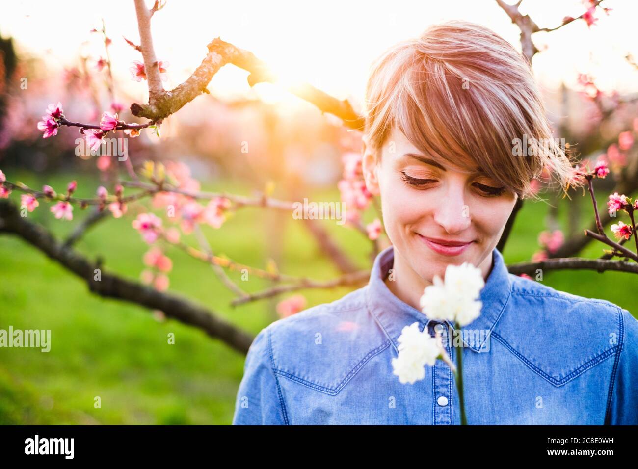 Primo piano di una donna sorridente che guarda i fiori nel parco durante tramonto Foto Stock