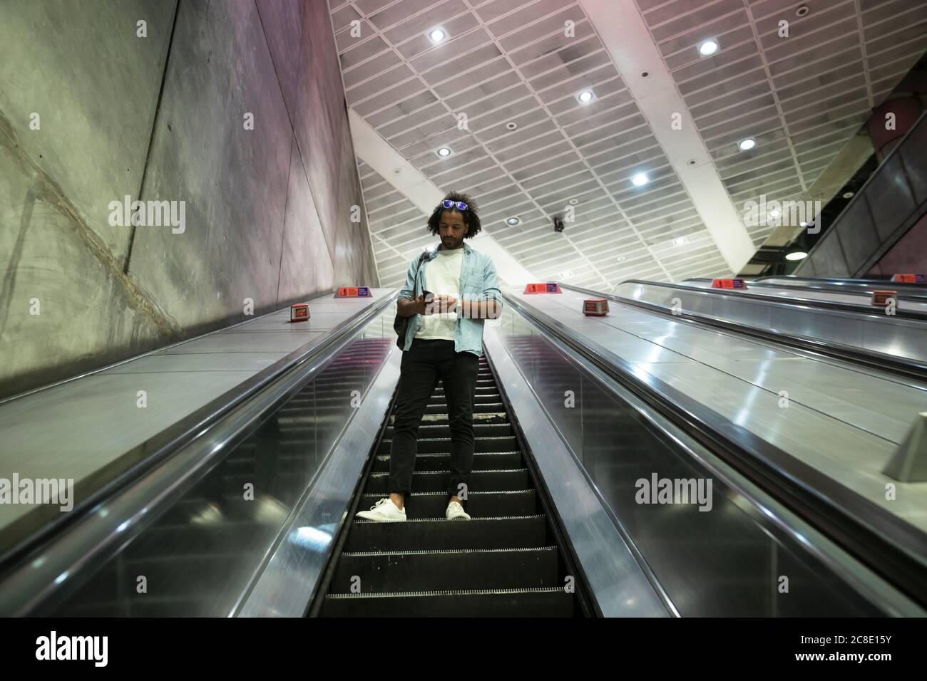 Giovane uomo alla moda che usa lo smartphone sulla scala mobile della metropolitana stazione Foto Stock