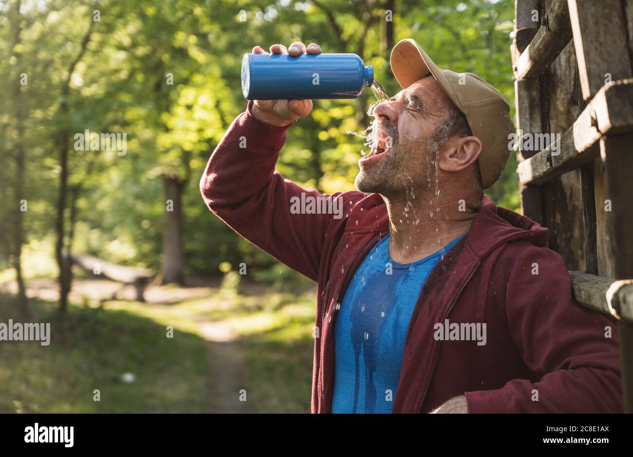 Uomo maturo che versa acqua sul viso dalla bottiglia al parco Foto Stock