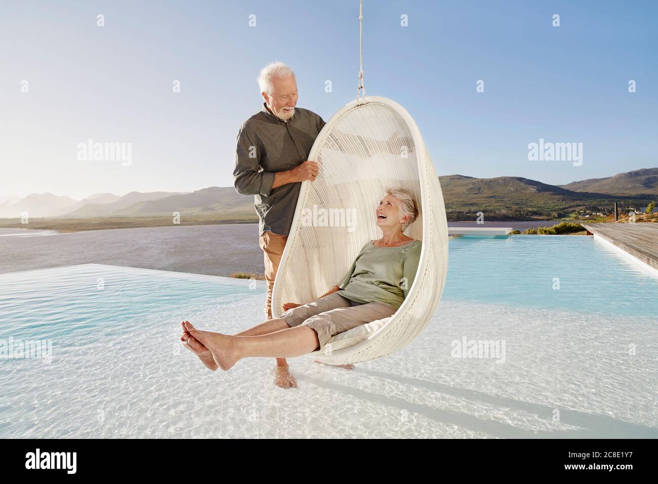Felice coppia anziana con donna seduta in sedia pensile sopra piscina Foto Stock