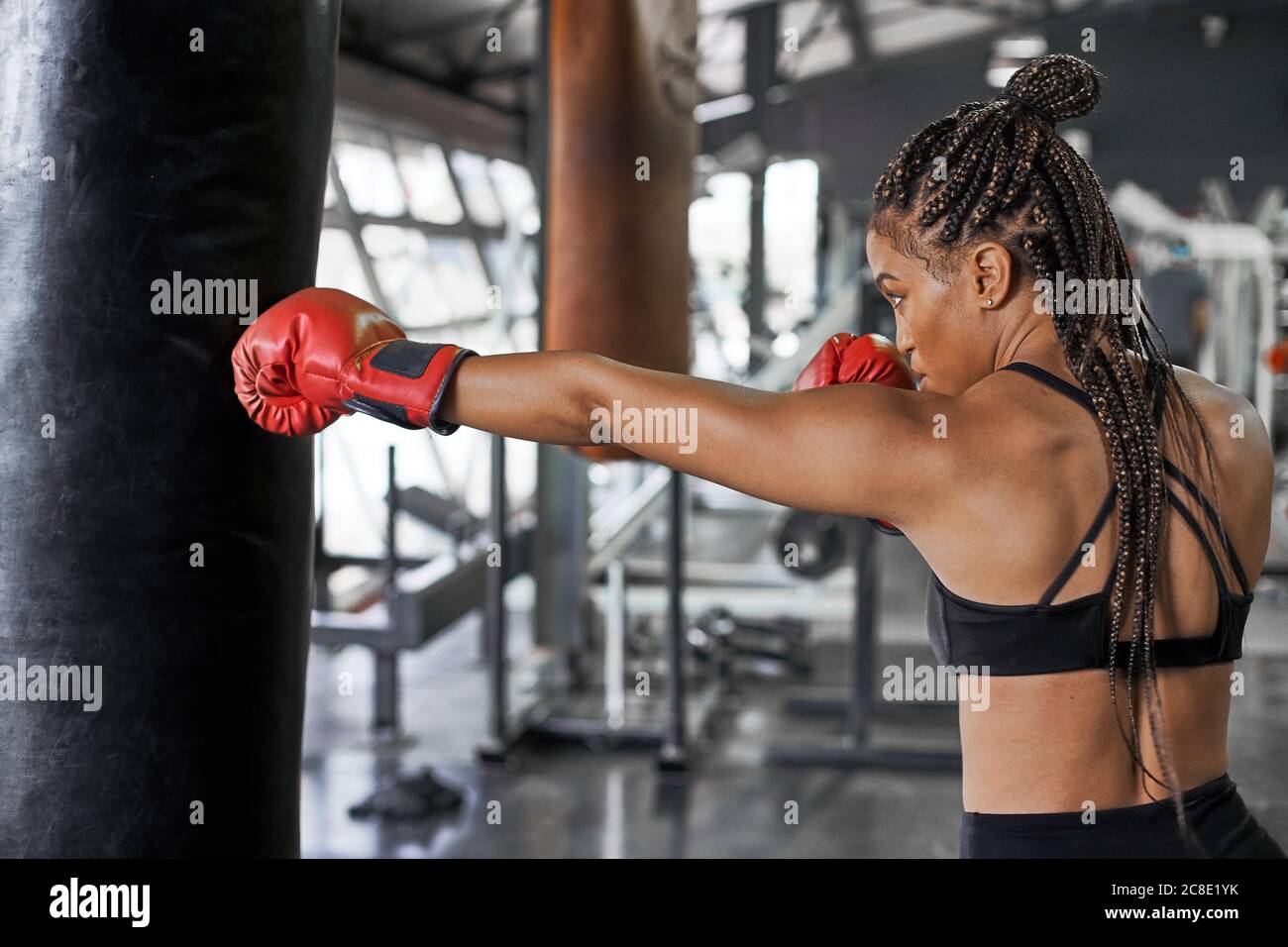 Atleta che indossa guanti rossi e pratica il pugilato sulla punzonatura borsa in palestra Foto Stock