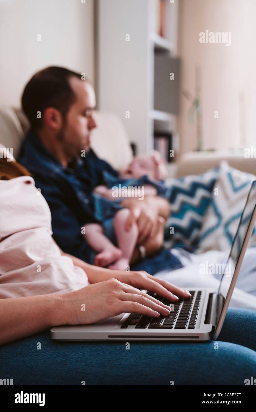 Madre che usa un computer portatile mentre il padre porta la figlia in background Foto Stock