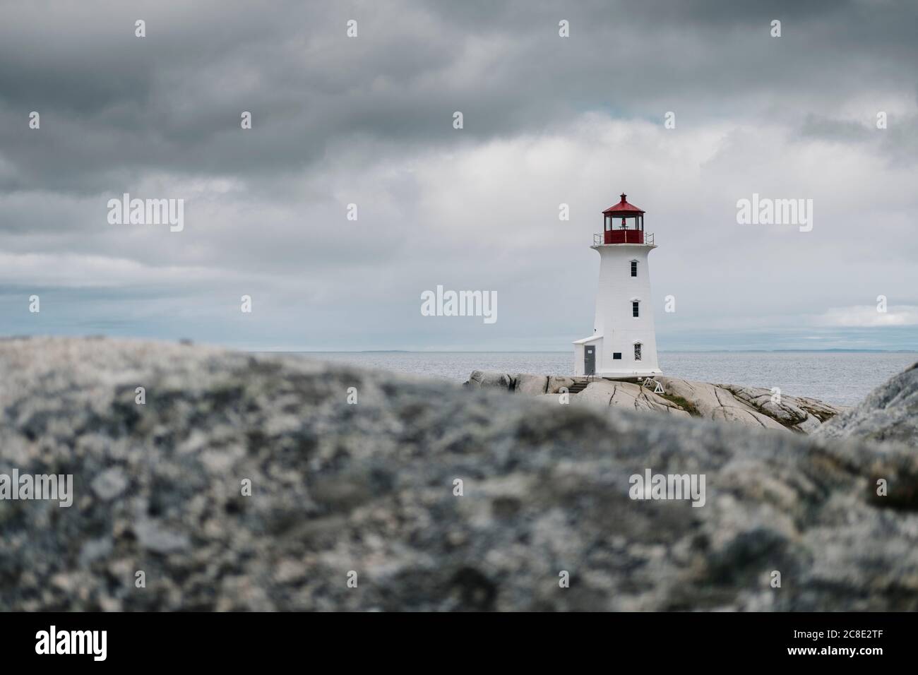 Faro di Peggys Point sulla formazione rocciosa dal mare contro il cielo nuvoloso, Nova Scotia, Canada Foto Stock