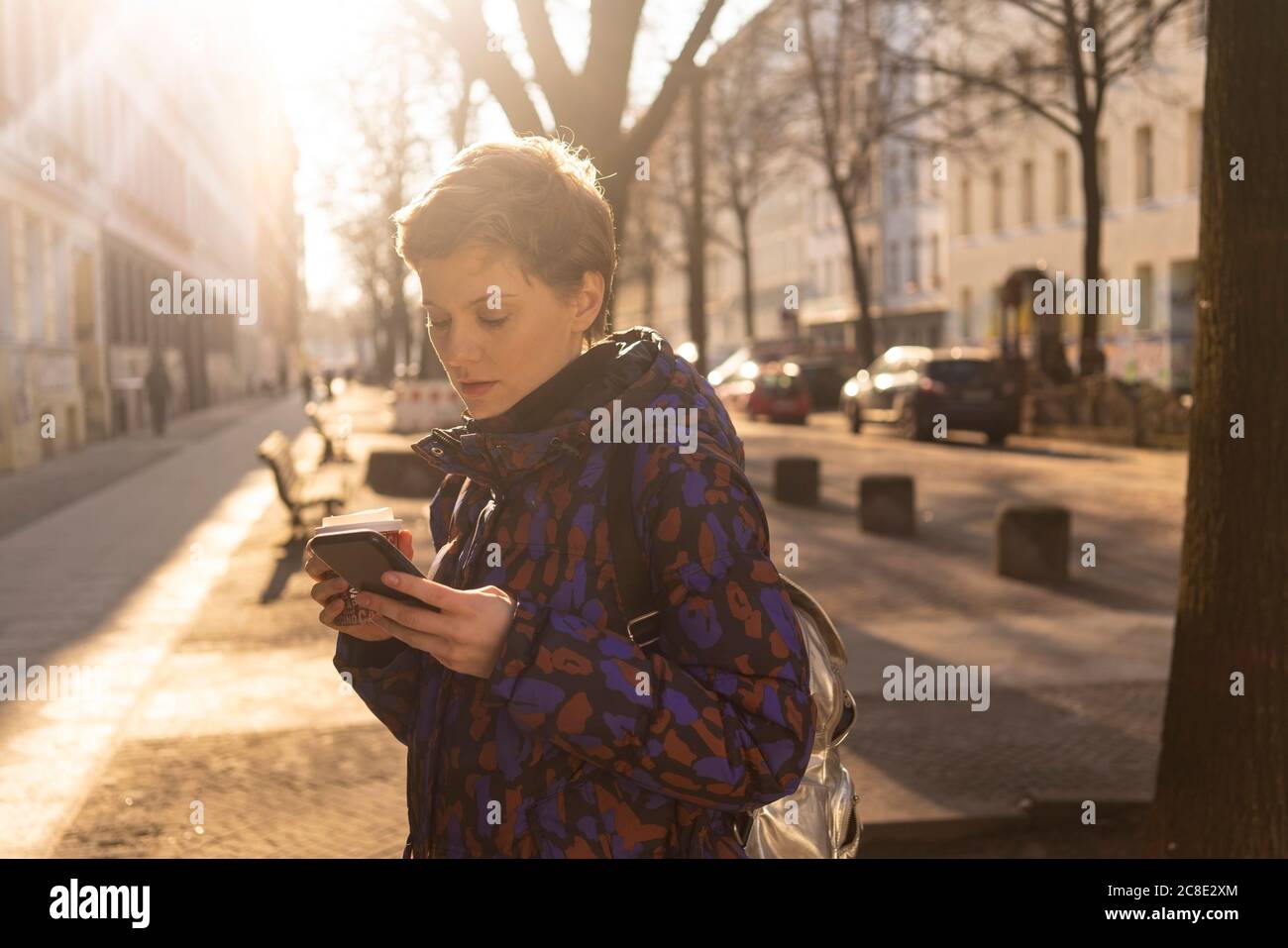 Ritratto di donna con zaino e caffè da andare guardando cellulare in serata, Berlino, Germania Foto Stock