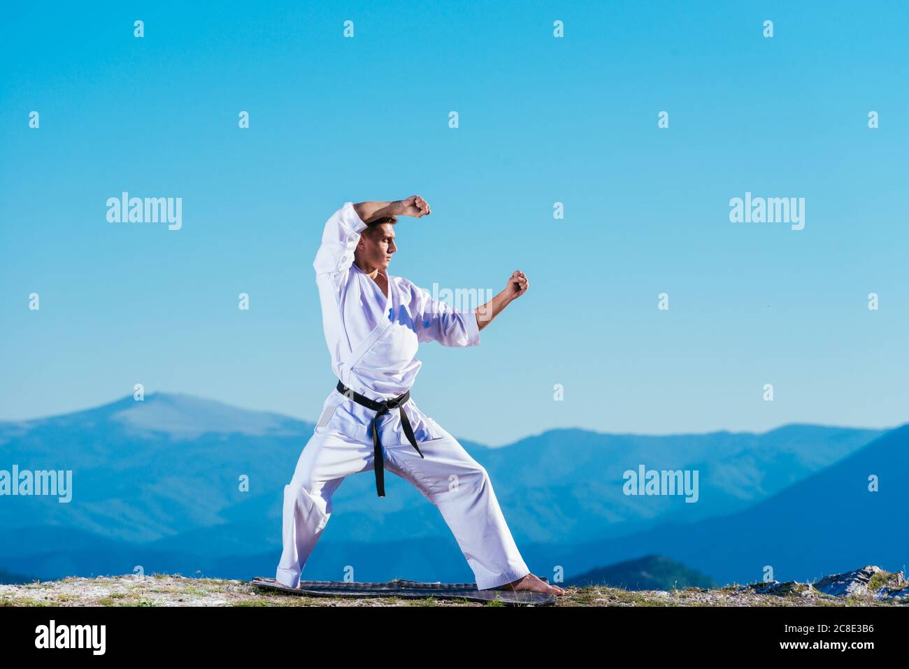 Bionda atleta di karate non kata sulla cima di una montagna mentre si esegue una linea di calci, pugni e blocchi sulla cima di una montagna in una giornata di sole. Foto Stock