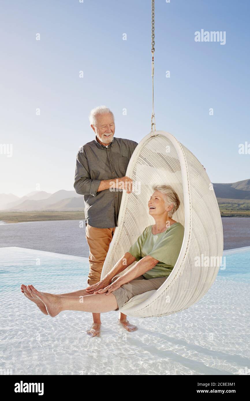 Felice coppia anziana con donna seduta in sedia pensile sopra piscina Foto Stock