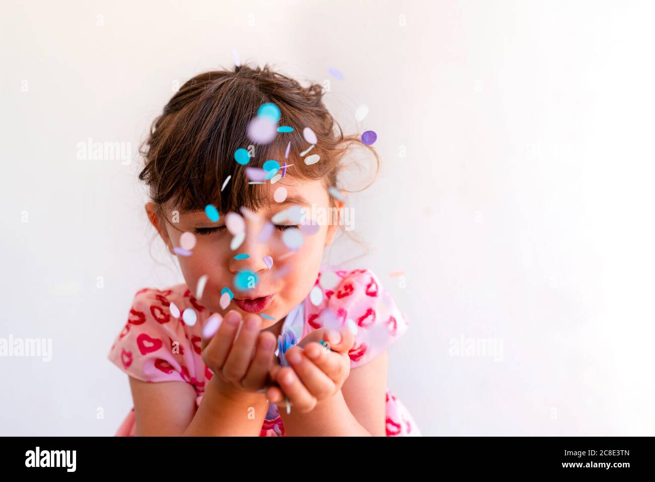 Primo piano di cute ragazza che soffia i confetti dalle mani contro il bianco sfondo Foto Stock
