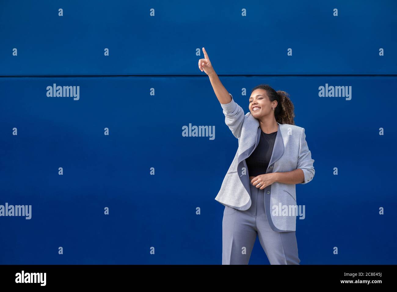 Donna d'affari sorridente con braccio rialzato di fronte alla parete blu Foto Stock