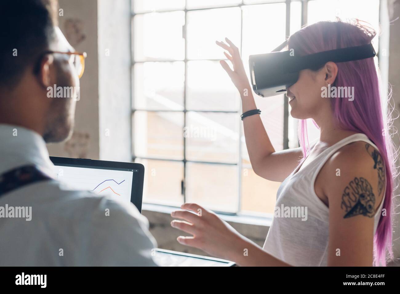 Due persone creative con occhiali di protezione per la realtà virtuale e laptop in loft ufficio Foto Stock