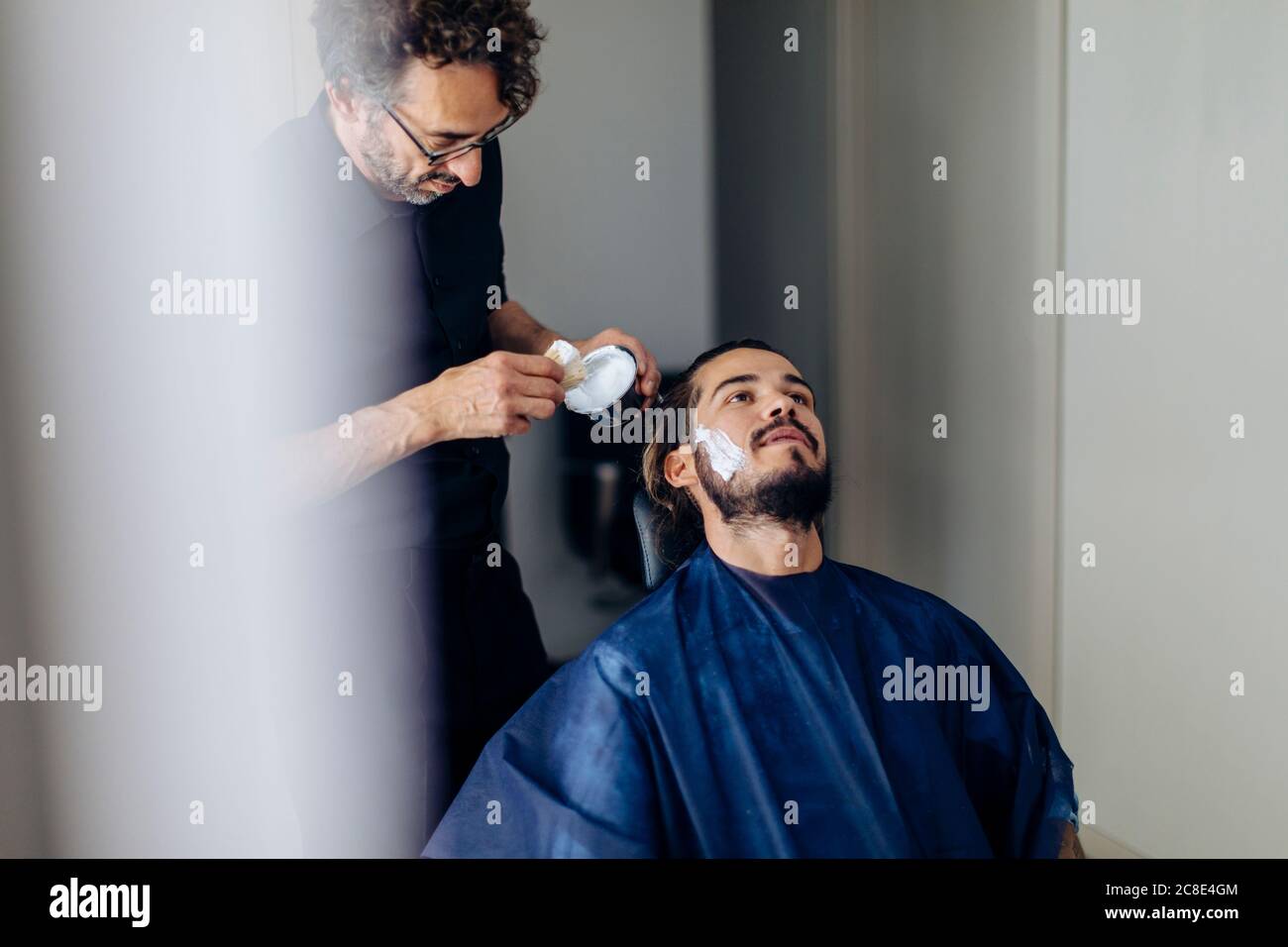 Barbiere che applica la crema da barba al cliente in salone Foto Stock