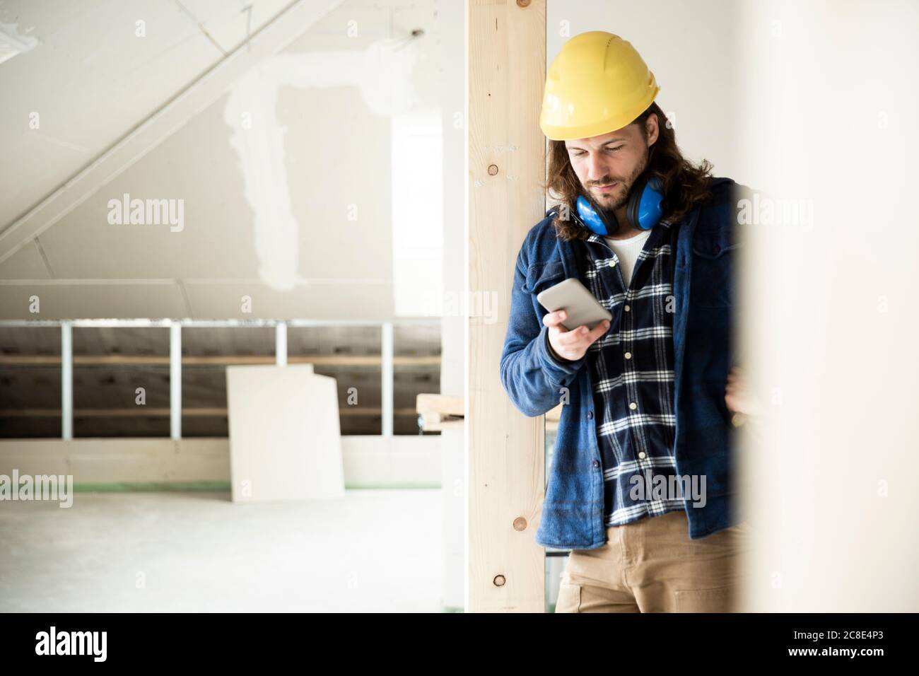Lavoratori edili che indossano il casco utilizzando lo smartphone mentre si è in piedi legno in casa ristrutturante Foto Stock