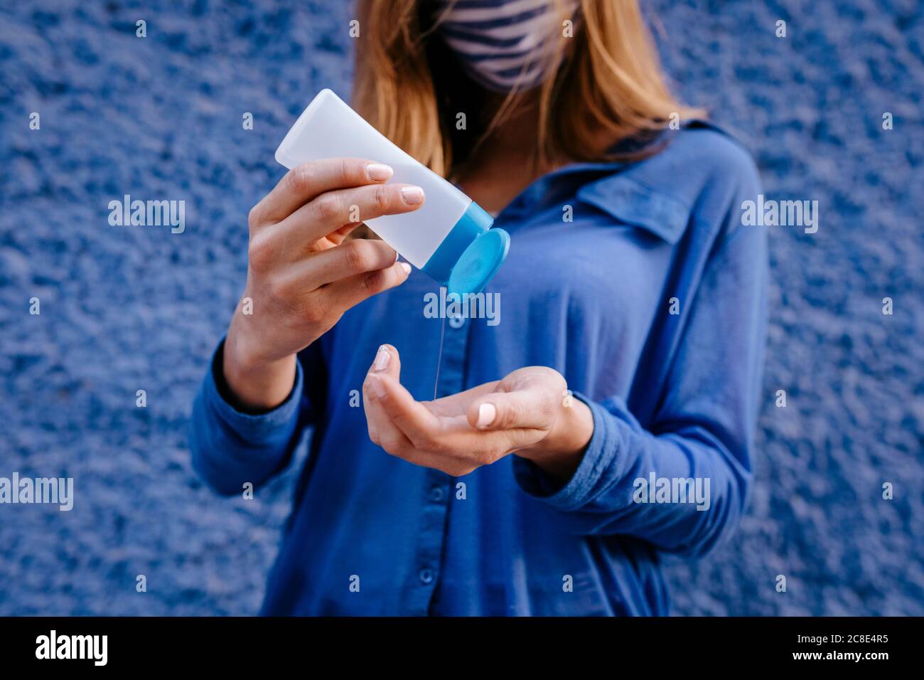 Primo piano di una giovane donna che lava le mani con l'igienizzatore contro il blu muro in città Foto Stock