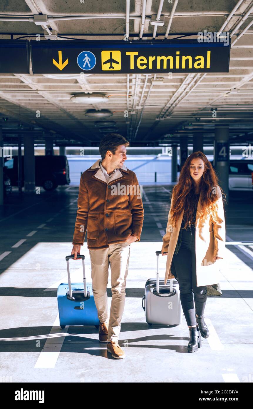 Una coppia di lavoro che tira i bagagli mentre cammina sotto il cartello del terminal aeroporto Foto Stock