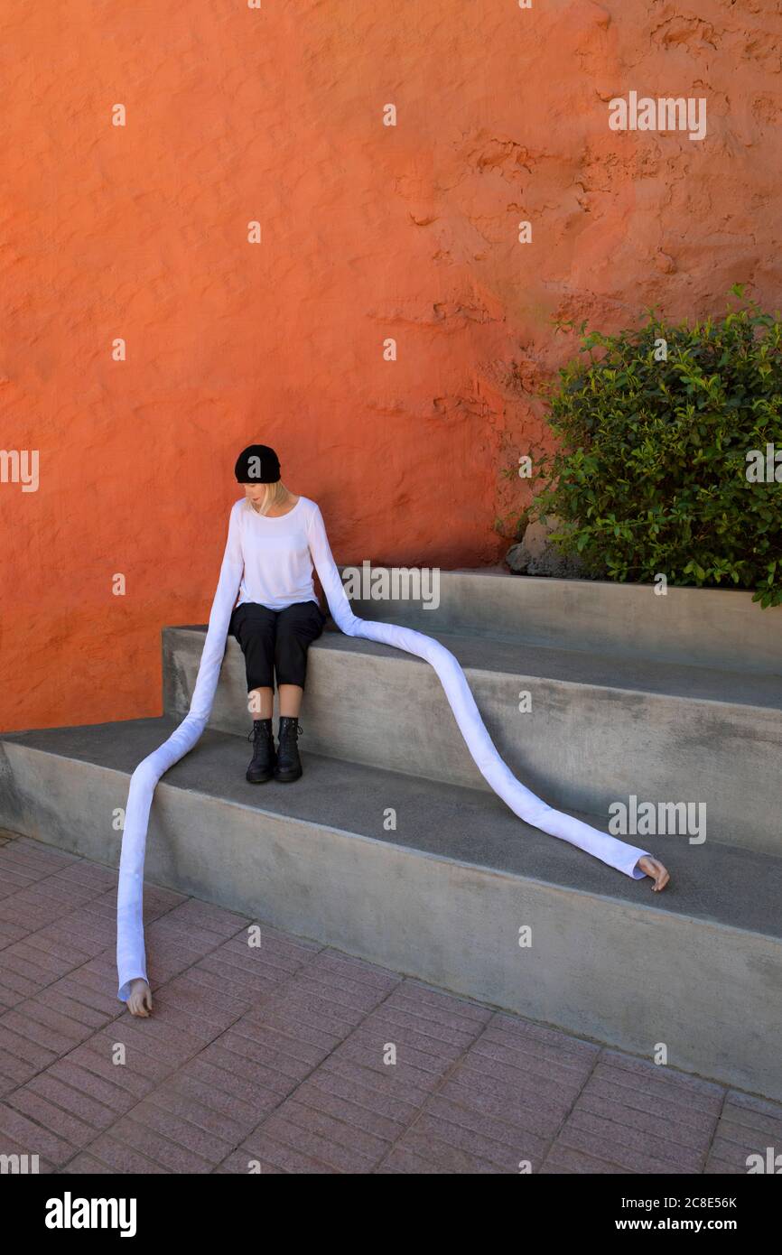Donna con mani lunghe artificiali seduta su passi concreti vicino piante Foto Stock