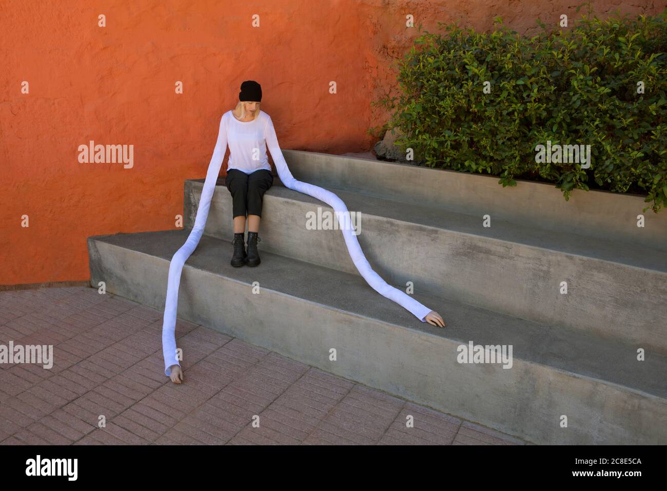 Donna con lunghe mani artificiali seduta su passi di cemento vicino piante Foto Stock