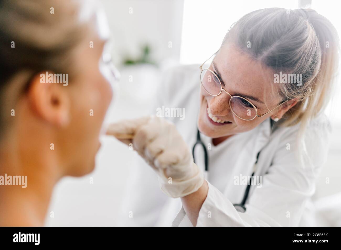 Medico femminile che esamina la paziente femminile con depressore della lingua Foto Stock