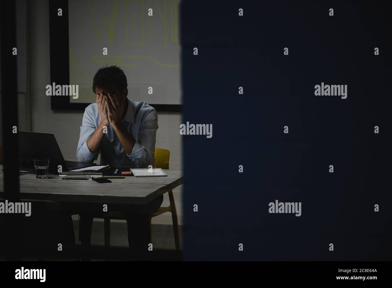 Uomo d'affari esausto che copre la faccia, seduto in ufficio, lavorando tardi Foto Stock