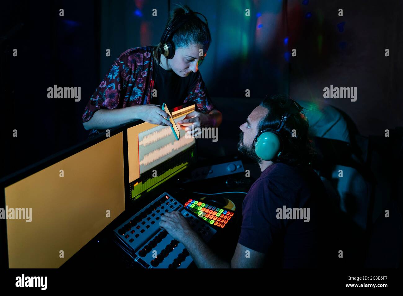 Donna che mostra smartphone a un uomo che utilizza il computer in registrazione studio a casa Foto Stock