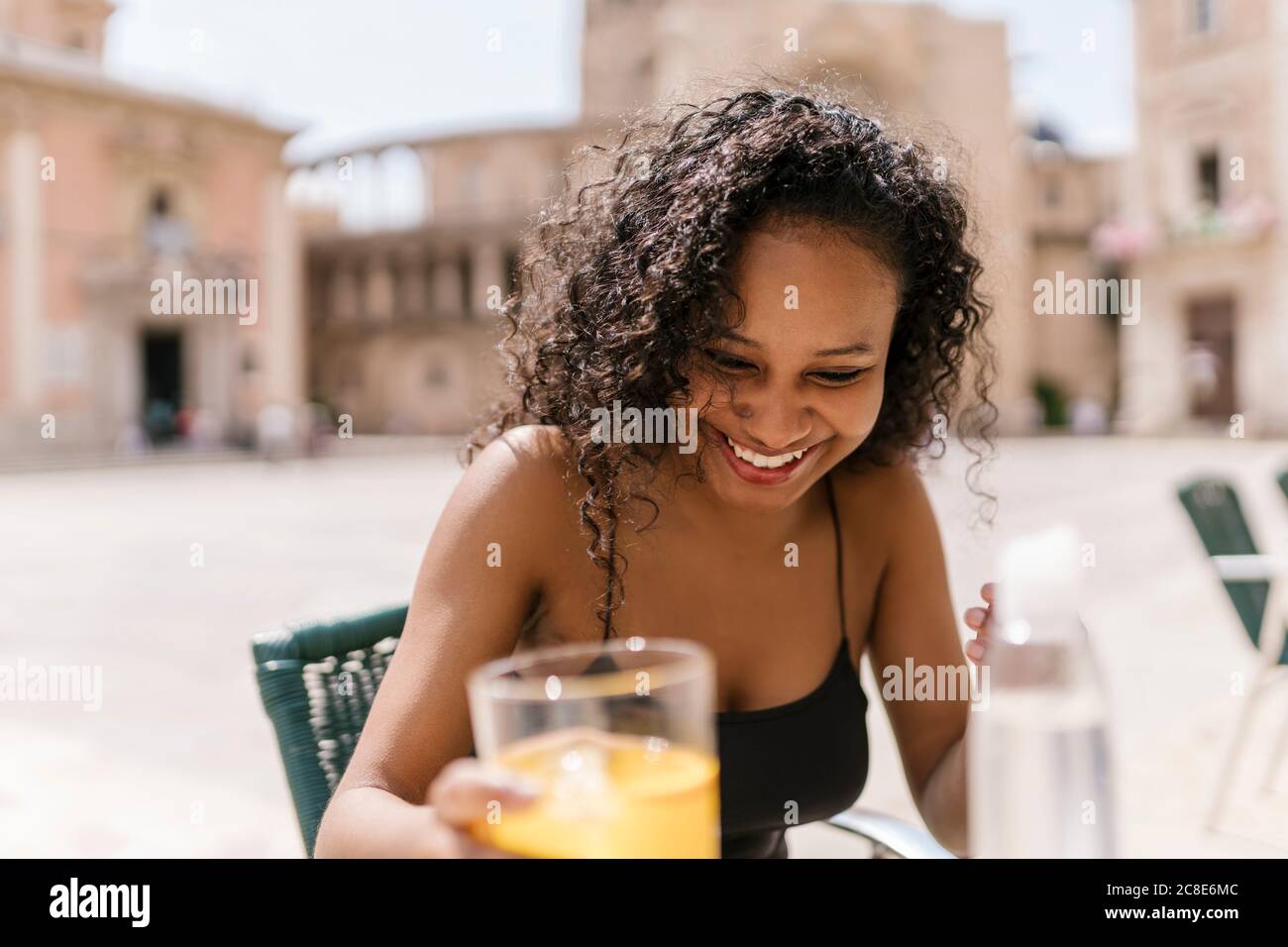 Donna felice che tiene un bicchiere di succo al bar sul marciapiede Foto Stock