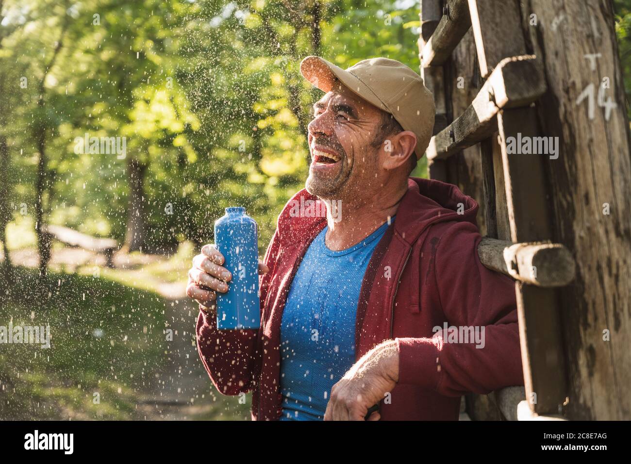 Uomo allegro in piedi da scala di legno con bottiglia d'acqua a. parcheggio Foto Stock