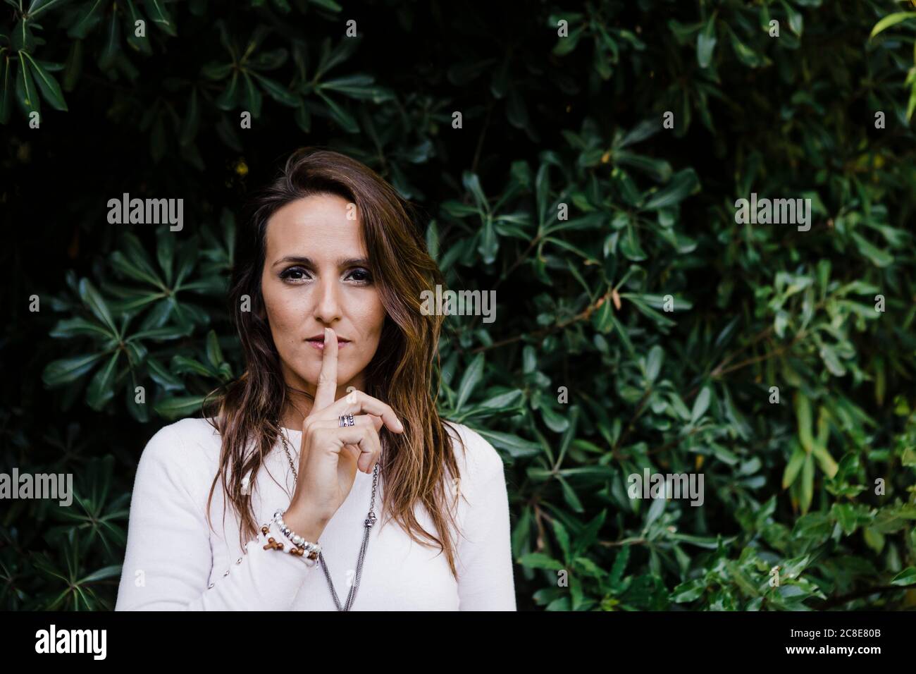 Bella donna con un dito sulle labbra contro le piante al parco Foto Stock