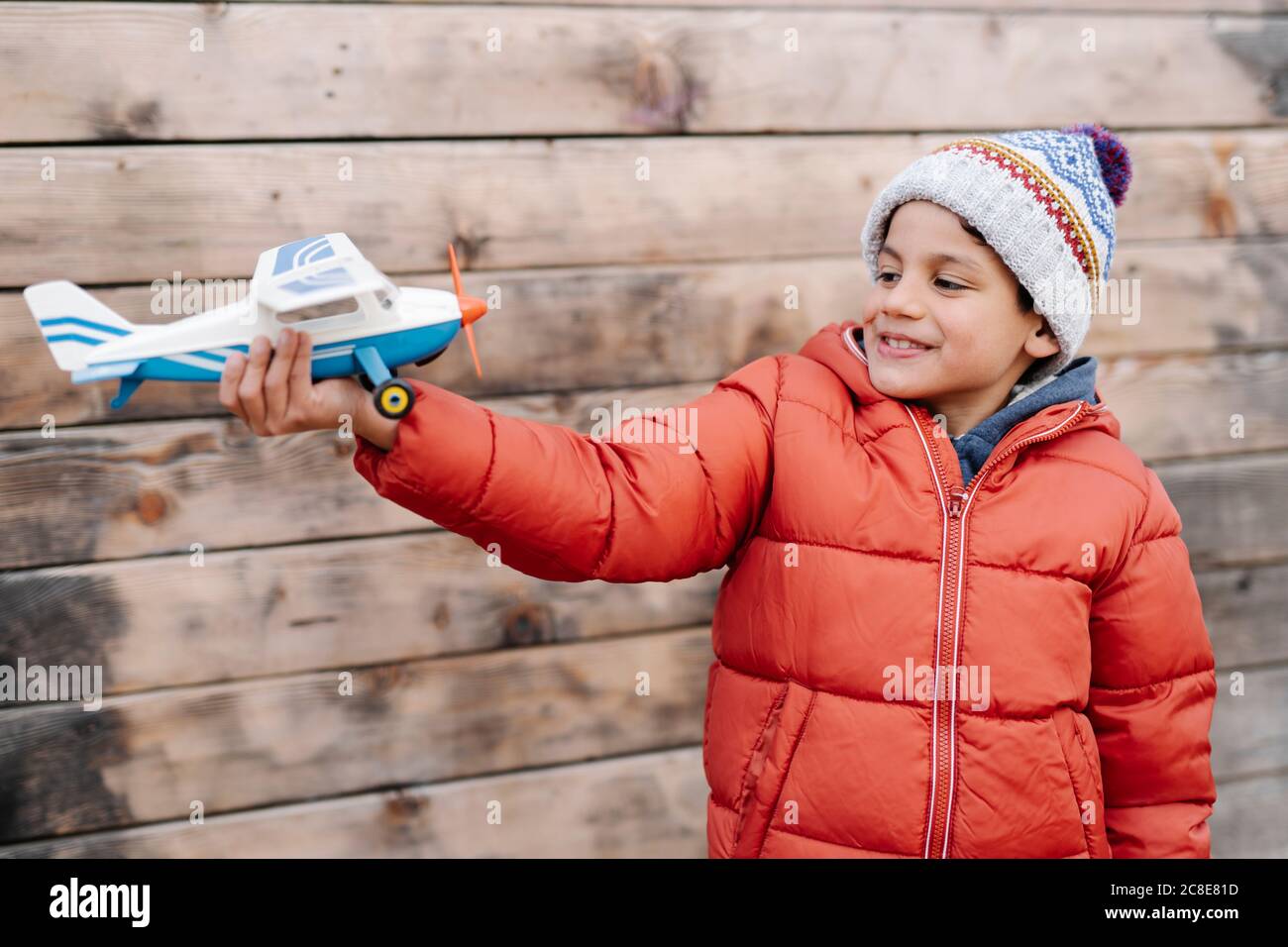 Ragazzo sorridente che indossa abiti caldi che tengono un aereo modello mentre si è in piedi contro muro Foto Stock