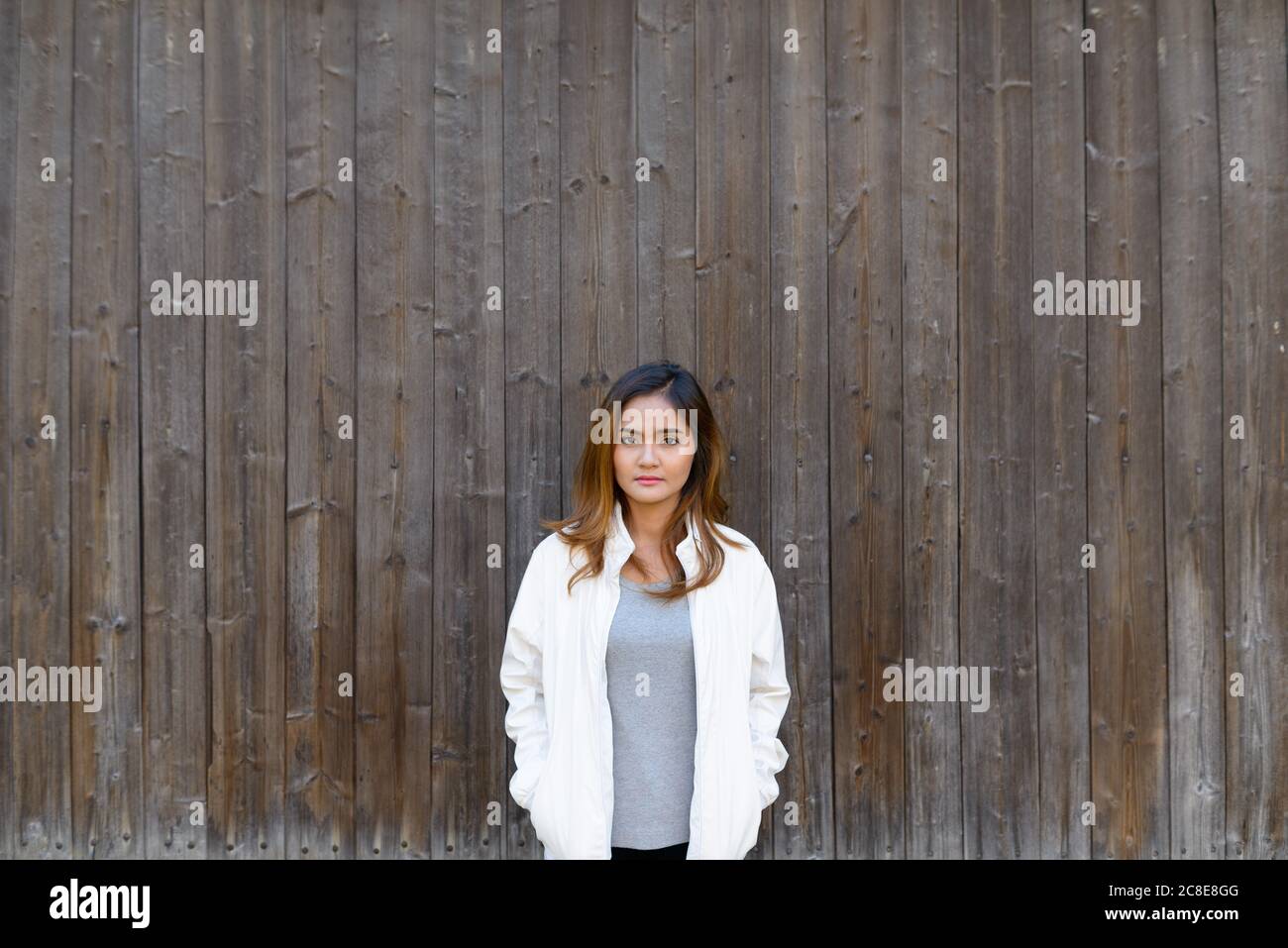 Giovane bella donna asiatica in piedi contro muro di legno Foto Stock