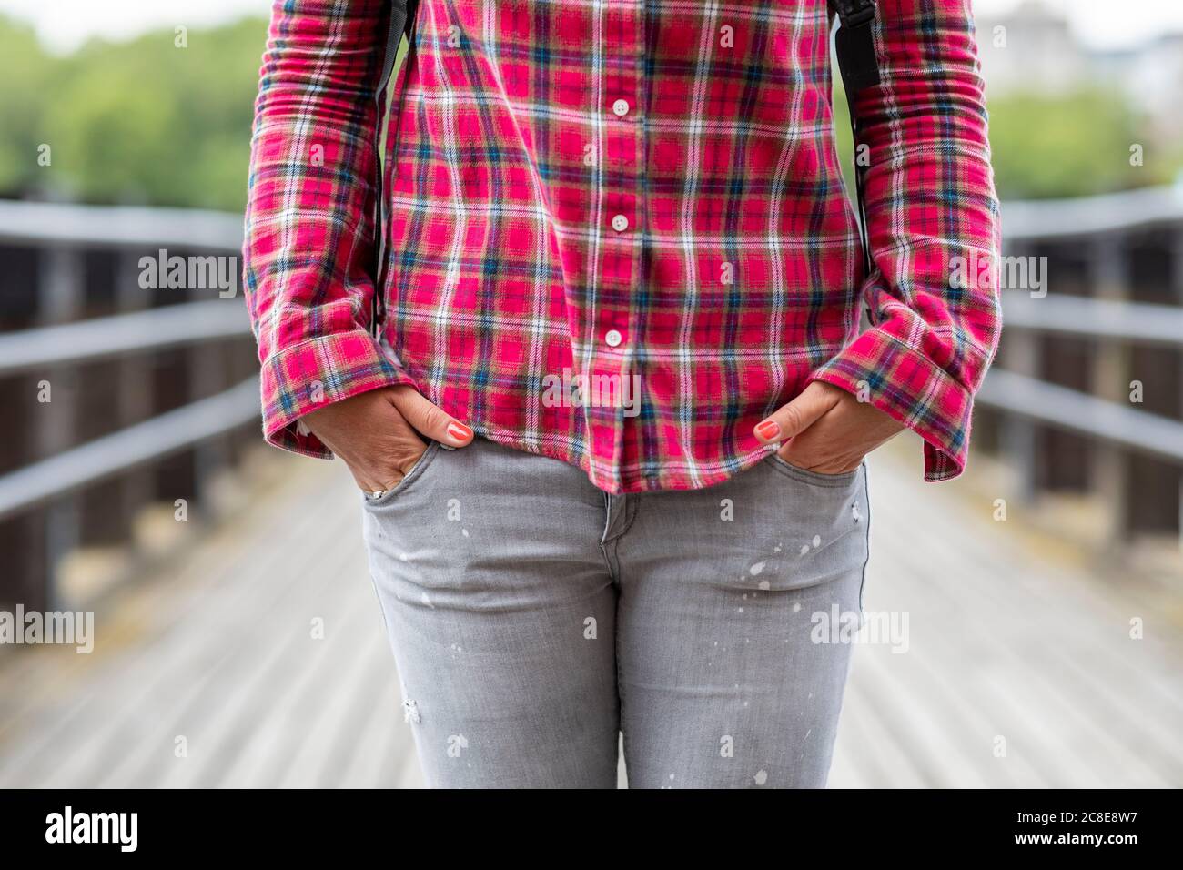 Primo piano di una donna che indossa una camicia controllata con le mani in tasca in piedi sul ponte Foto Stock