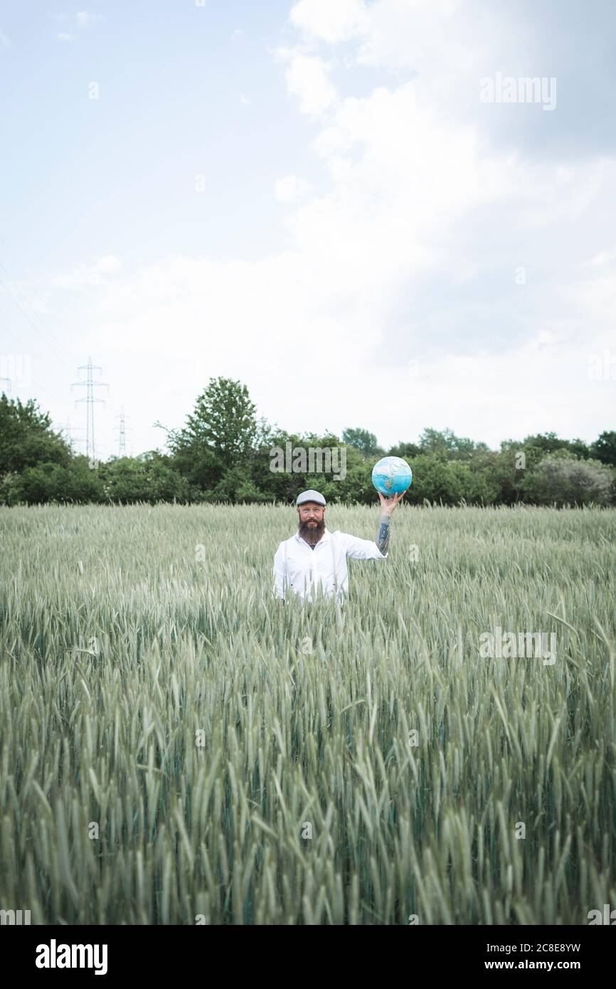 Uomo maturo che tiene il globo mentre sta in mezzo al cornfield contro il cielo Foto Stock