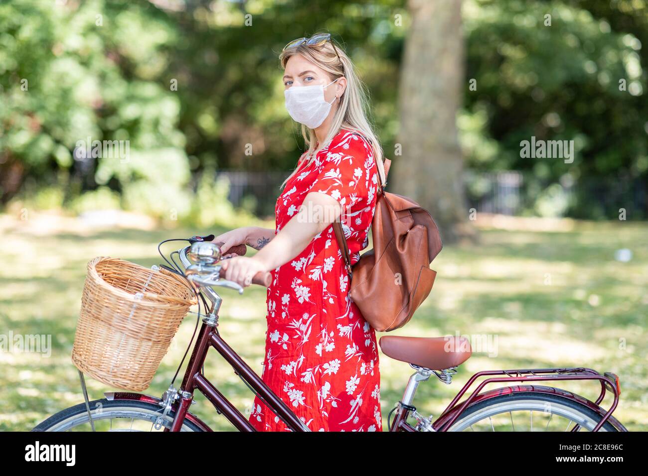 Donna mid adult che indossa la maschera mentre si è in piedi con la bicicletta dentro parco pubblico Foto Stock