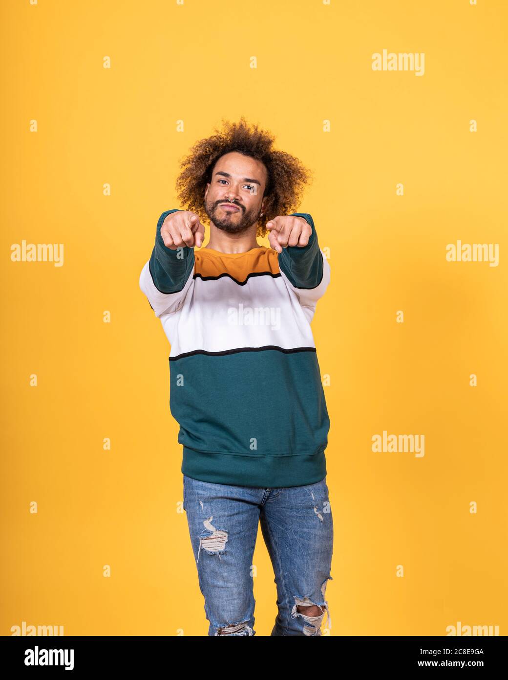 Bell'uomo giovane con capelli ricci che puntano mentre si sta in piedi contro sfondo giallo Foto Stock