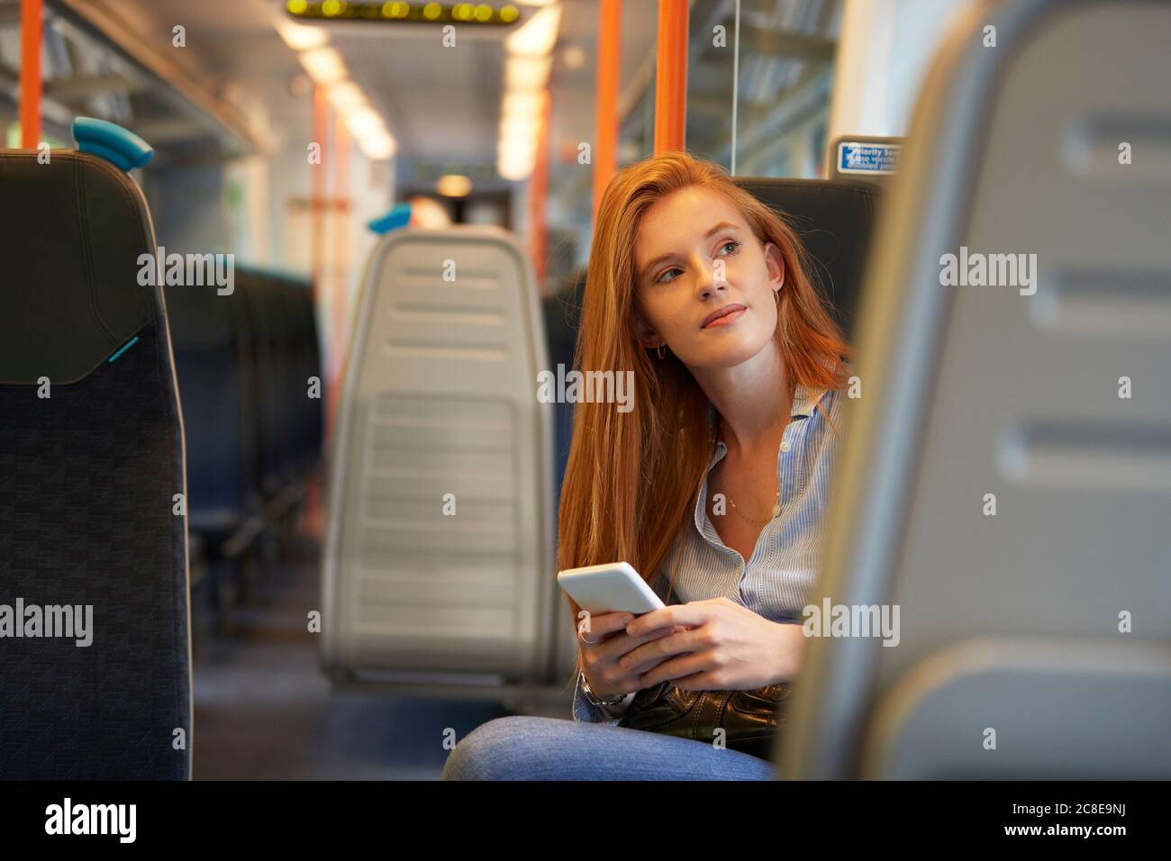 Donna premurosa che tiene lo smartphone mentre si siede in treno Foto Stock