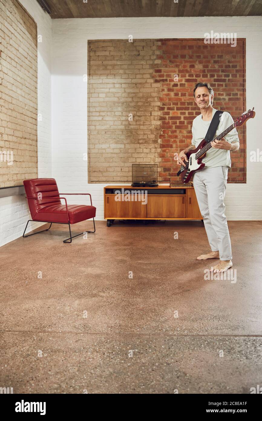 Uomo anziano che suona la chitarra basso in un piano loft Foto Stock