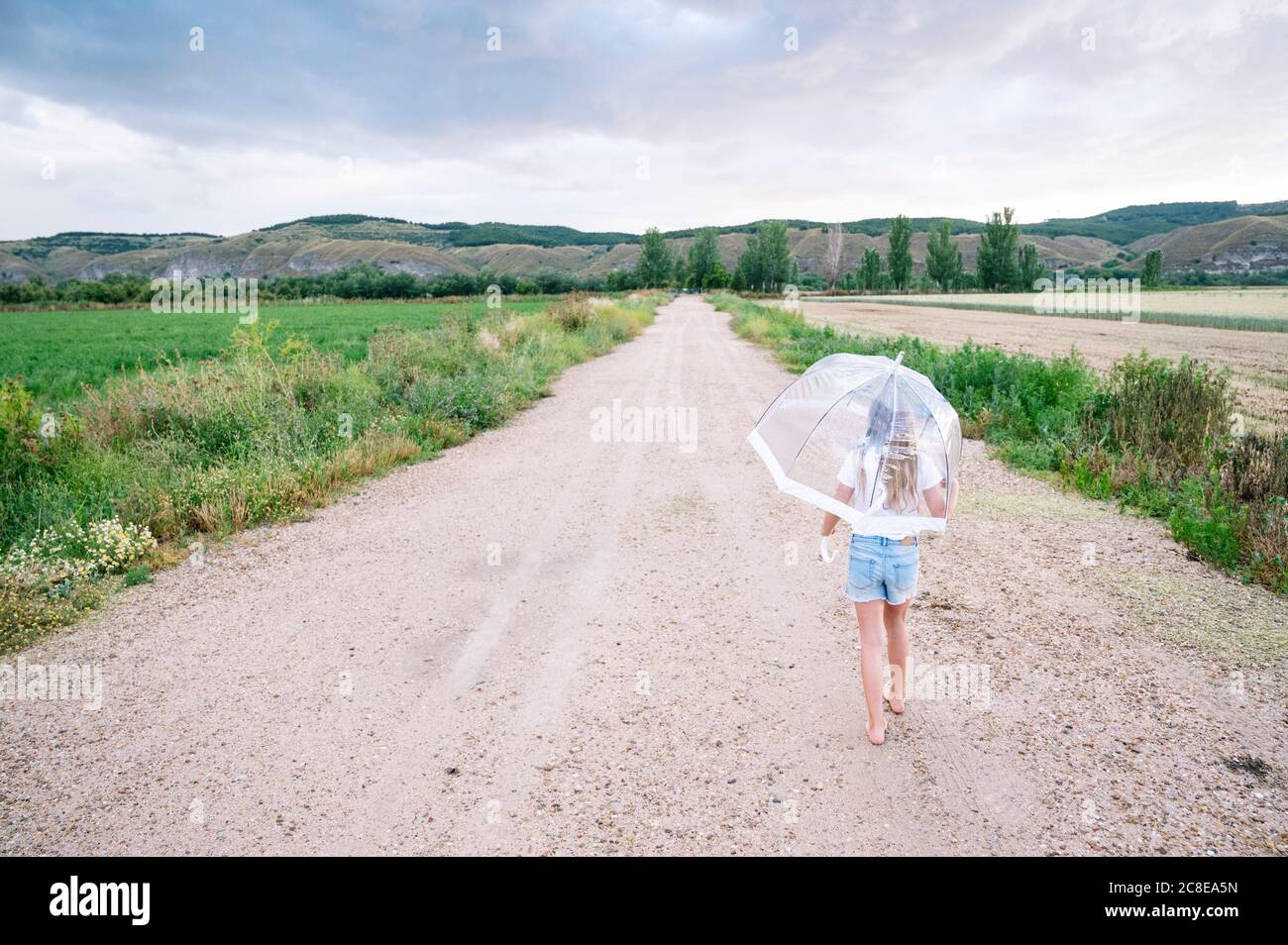 Ragazza con ombrello che cammina su strada sterrata durante il monsone Foto Stock